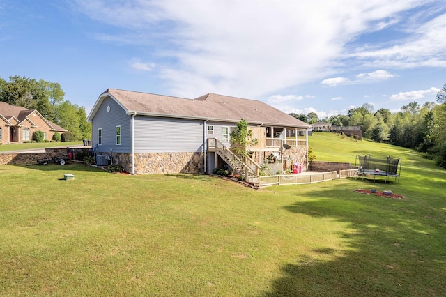 rear view of property featuring a trampoline, stairs, central AC unit, a yard, and stone siding