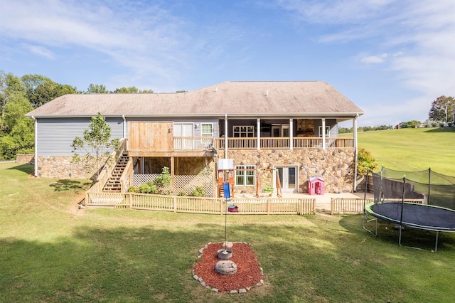 rear view of house featuring a yard, stone siding, stairs, and a trampoline