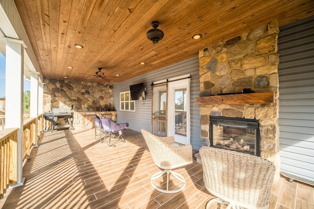 wooden deck featuring a grill, an outdoor stone fireplace, and a ceiling fan