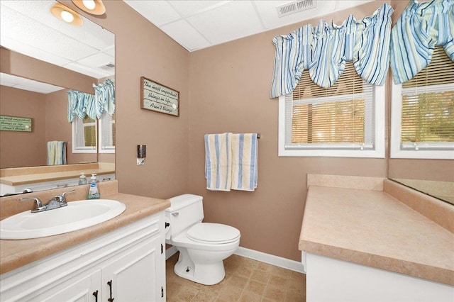  - bathroom with visible vents, vanity, baseboards, toilet, and a drop ceiling