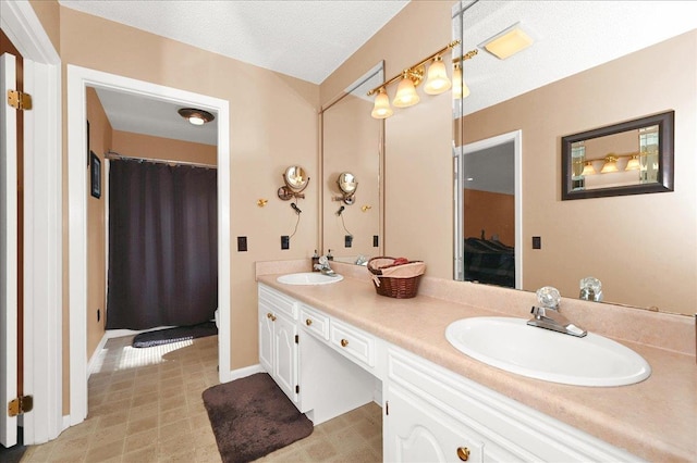  - bathroom with baseboards, double vanity, a textured ceiling, and a sink