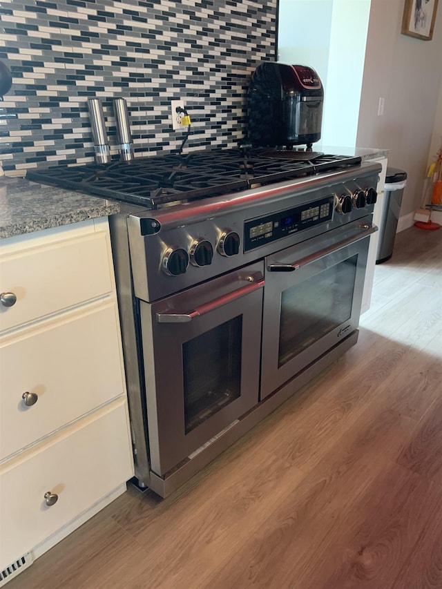 kitchen with tasteful backsplash, white cabinets, dark stone counters, range with two ovens, and light wood-style floors