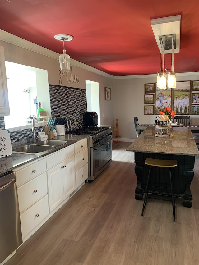 kitchen with stainless steel appliances, a sink, white cabinets, dark countertops, and pendant lighting