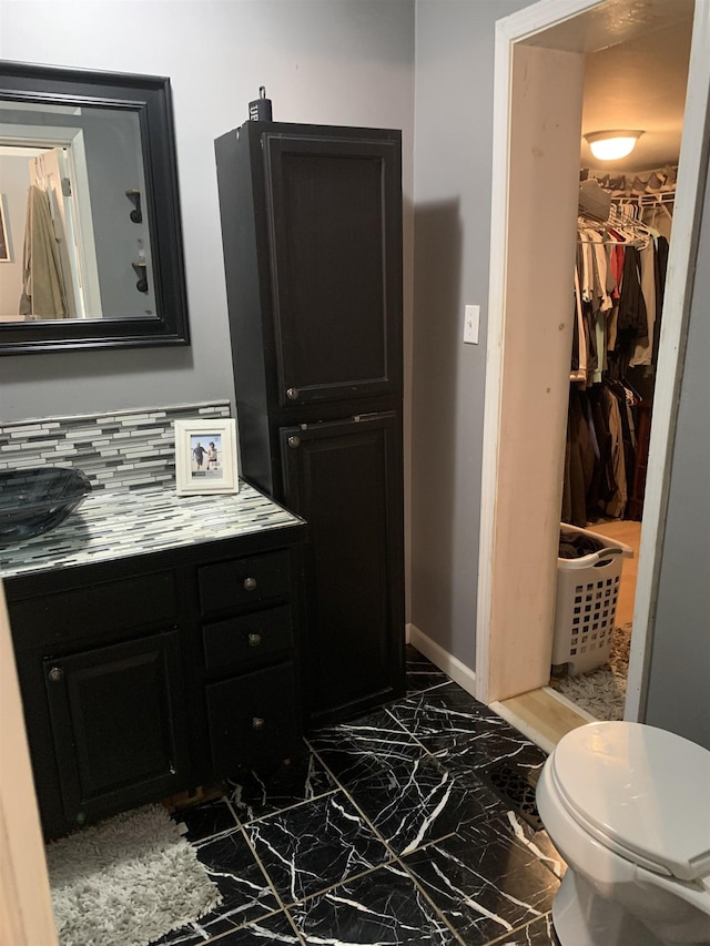 bathroom with marble finish floor, a spacious closet, baseboards, and vanity