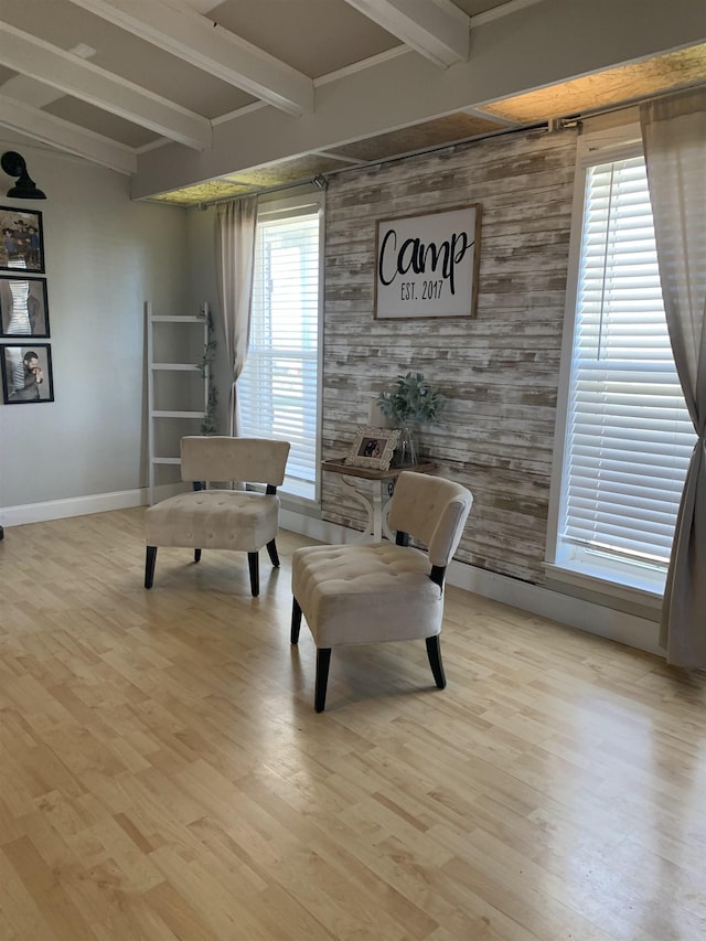 sitting room featuring light wood-style floors, an accent wall, baseboards, and beam ceiling