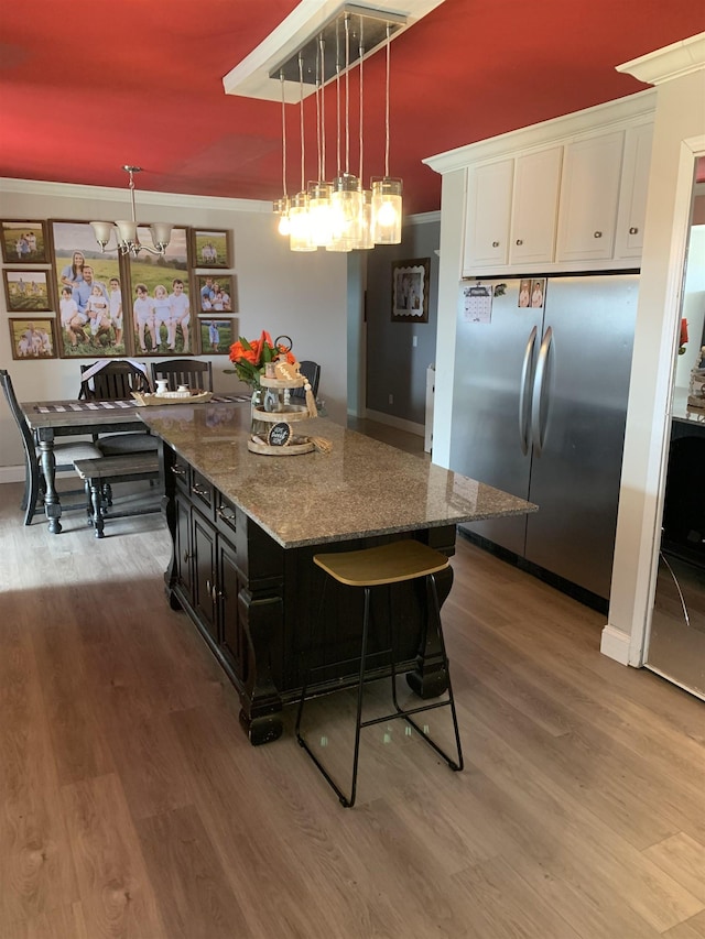 kitchen with pendant lighting, crown molding, a breakfast bar area, freestanding refrigerator, and a kitchen island