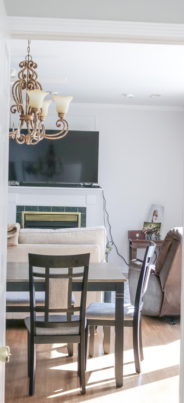 dining area with hardwood / wood-style flooring, crown molding, a fireplace, and a chandelier