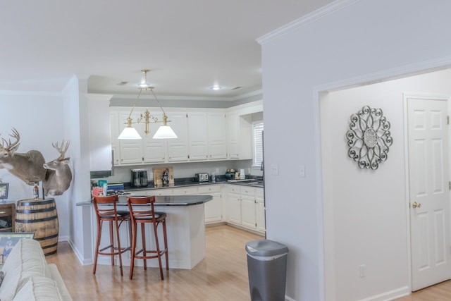 kitchen with crown molding, a breakfast bar, white cabinets, kitchen peninsula, and light wood-type flooring