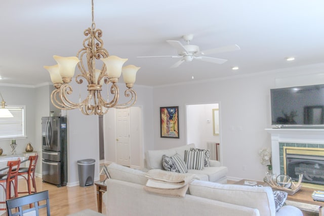 living room with crown molding, light hardwood / wood-style flooring, a tile fireplace, and ceiling fan with notable chandelier