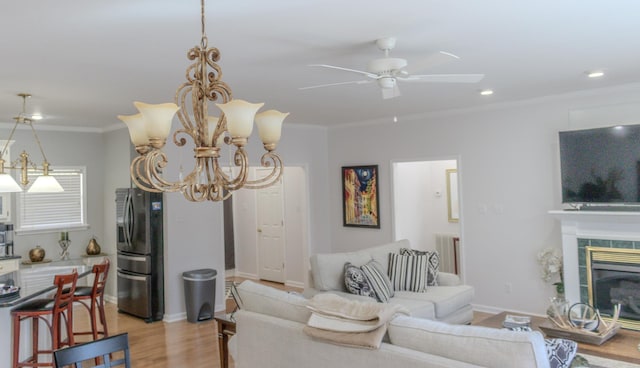 living room featuring ceiling fan with notable chandelier, a fireplace, ornamental molding, and light wood-type flooring