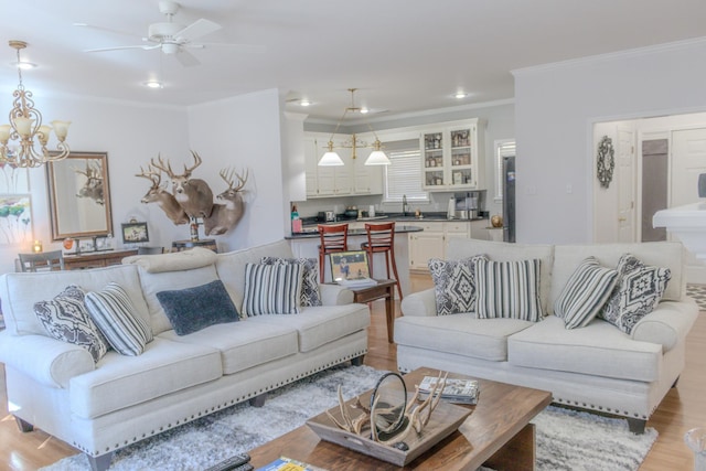 living room with crown molding, sink, ceiling fan with notable chandelier, and light wood-type flooring