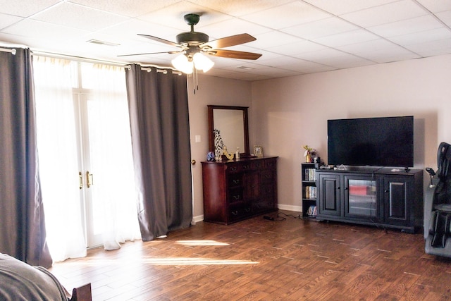 living room with a drop ceiling, dark wood-type flooring, and ceiling fan