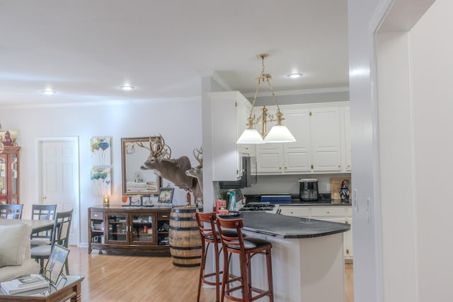 kitchen featuring white cabinetry, ornamental molding, a kitchen breakfast bar, pendant lighting, and light hardwood / wood-style floors