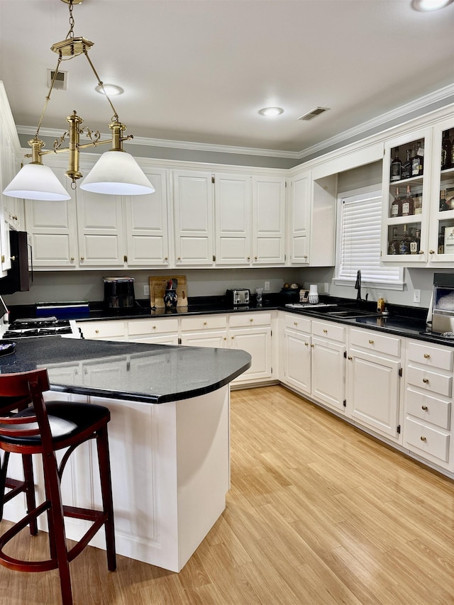 kitchen with a breakfast bar, ornamental molding, white cabinets, decorative light fixtures, and light wood-type flooring