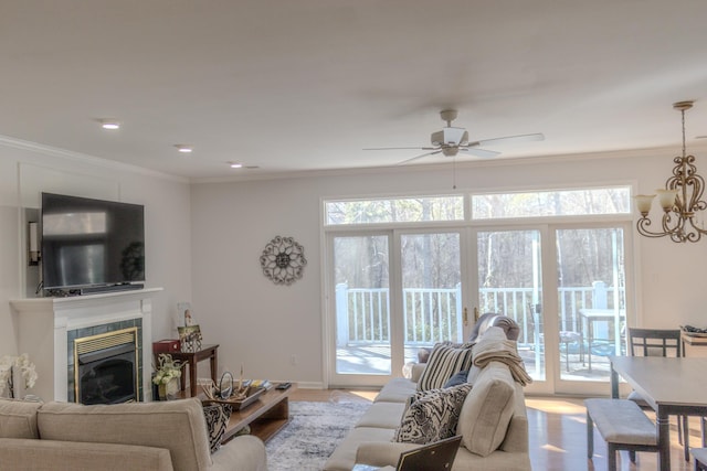 living room with ornamental molding, ceiling fan with notable chandelier, a tile fireplace, and light wood-type flooring