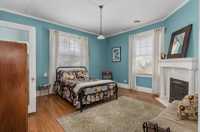bedroom featuring visible vents, ornamental molding, wood finished floors, baseboards, and a tile fireplace