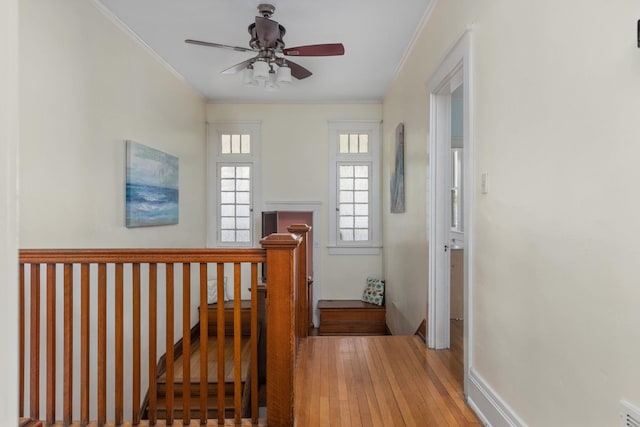 hall with visible vents, crown molding, baseboards, wood-type flooring, and an upstairs landing