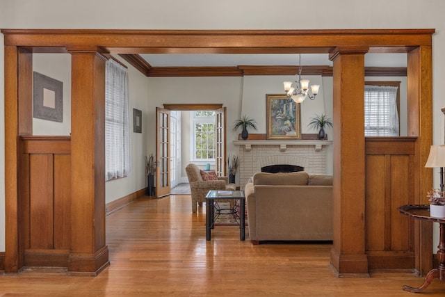 living area featuring a brick fireplace, a chandelier, baseboards, wood finished floors, and ornamental molding