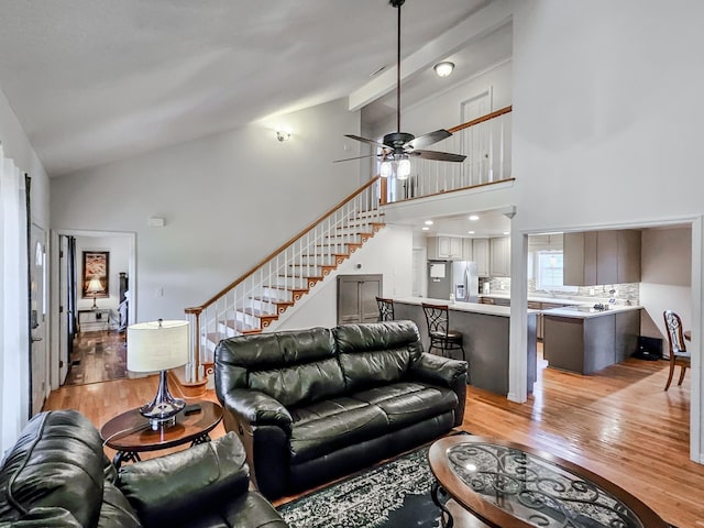 living room featuring beamed ceiling, ceiling fan, light wood-type flooring, and high vaulted ceiling