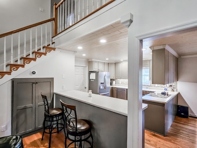 kitchen featuring gray cabinetry, stainless steel appliances, decorative backsplash, a breakfast bar, and light wood-type flooring