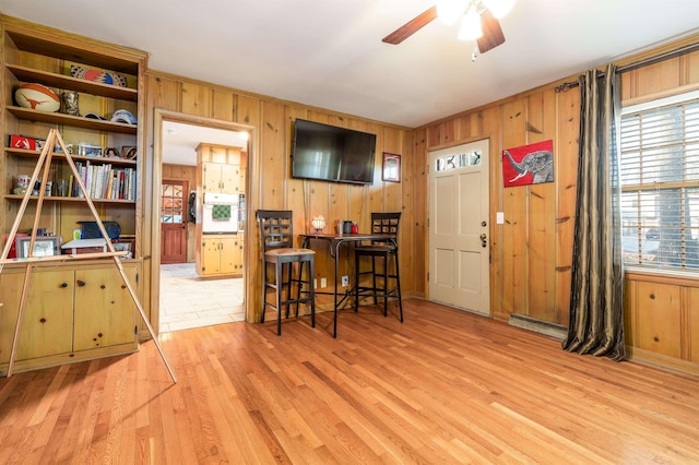 interior space featuring light wood-style floors, ceiling fan, and wood walls