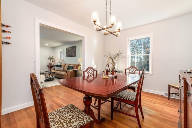 dining space with light wood-type flooring, an inviting chandelier, visible vents, and baseboards