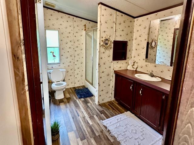  - bathroom with ornamental molding, wood finished floors, toilet, wallpapered walls, and a stall shower