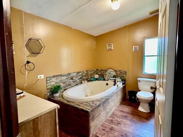  - bathroom featuring toilet, a tub with jets, wood finished floors, and lofted ceiling