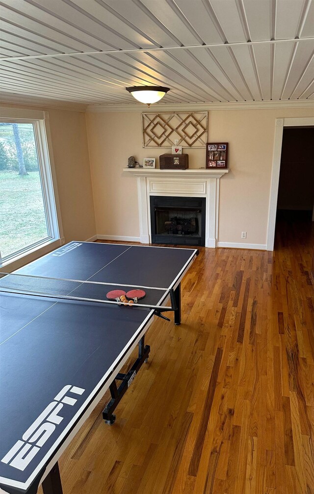 recreation room with ornamental molding, a fireplace, wood finished floors, and baseboards