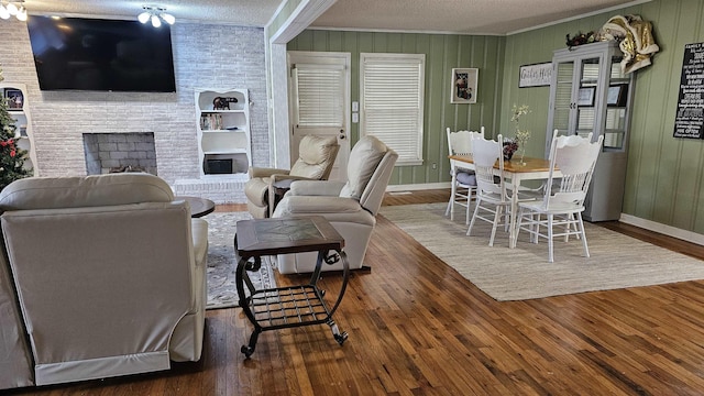 living room featuring a brick fireplace, crown molding, a textured ceiling, and wood finished floors