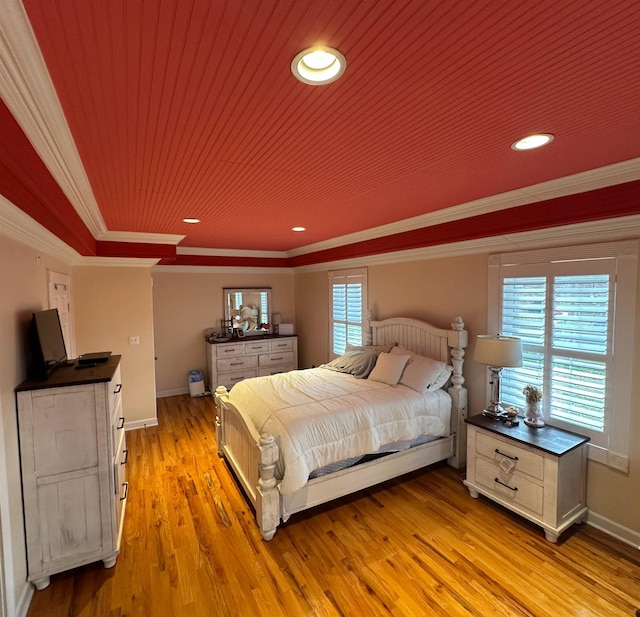 bedroom with ornamental molding, a tray ceiling, multiple windows, and light wood-style flooring