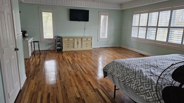 bedroom with a wainscoted wall, visible vents, and wood finished floors