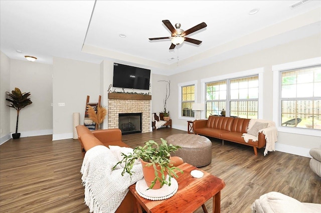 living room featuring a fireplace, wood-type flooring, a raised ceiling, and ceiling fan