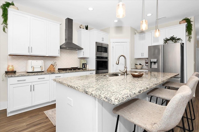 kitchen featuring wall chimney range hood, sink, appliances with stainless steel finishes, and an island with sink