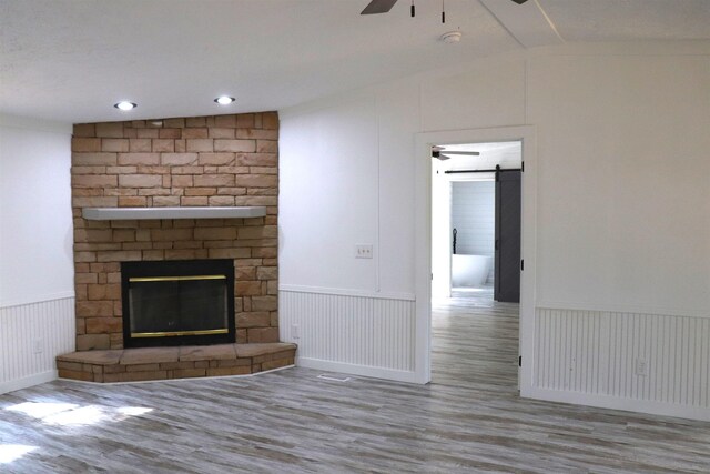  - unfurnished living room featuring a ceiling fan, lofted ceiling, a wainscoted wall, wood finished floors, and a fireplace