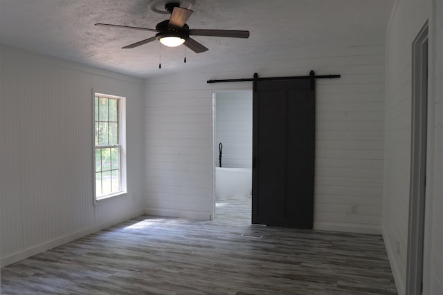  - unfurnished room with a textured ceiling, a barn door, a ceiling fan, and wood finished floors