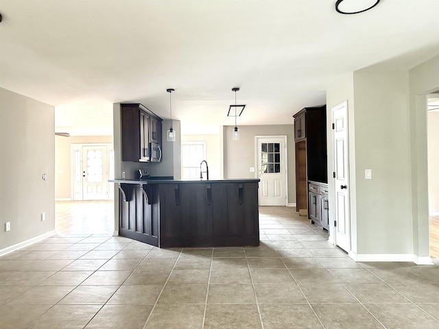 kitchen featuring pendant lighting, a kitchen breakfast bar, sink, light tile patterned flooring, and dark brown cabinetry