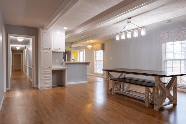 kitchen with beamed ceiling, white cabinetry, stainless steel fridge, and decorative light fixtures