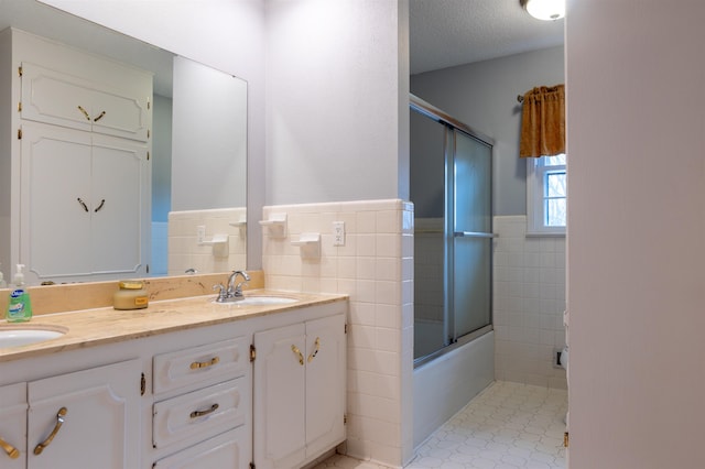 bathroom featuring vanity, shower / bath combination with glass door, tile walls, and a textured ceiling