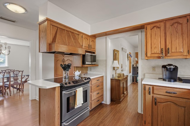 kitchen featuring decorative backsplash, appliances with stainless steel finishes, custom exhaust hood, a notable chandelier, and light hardwood / wood-style floors