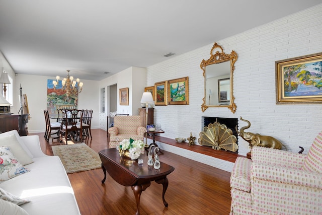 living room with a fireplace, hardwood / wood-style flooring, an inviting chandelier, and brick wall