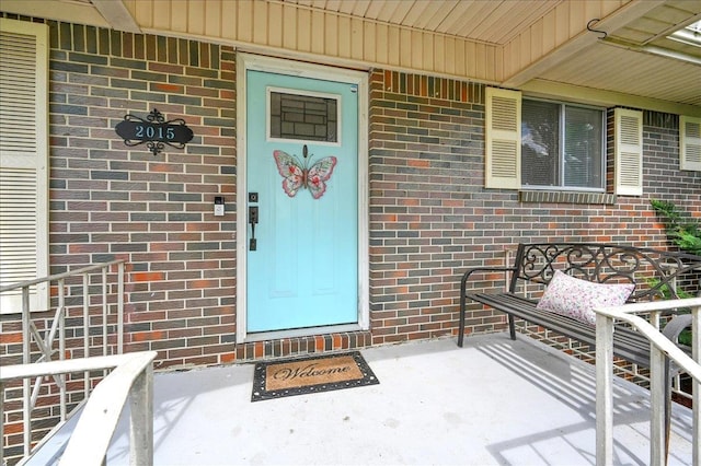  - doorway to property featuring brick siding and covered porch