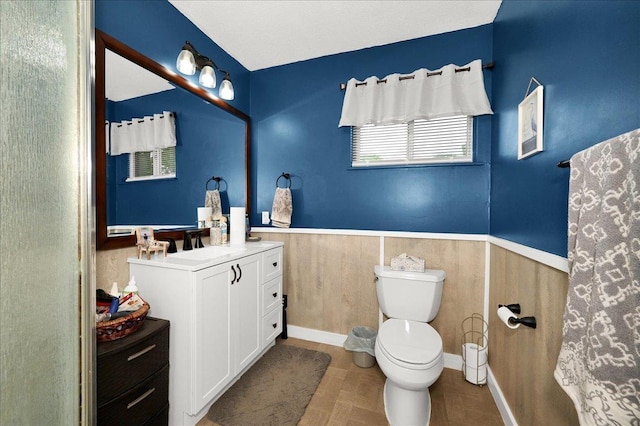  - full bath with toilet, vanity, a wainscoted wall, and baseboards