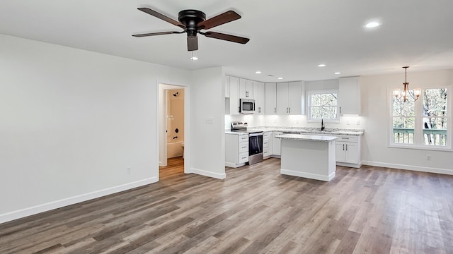 kitchen with stainless steel appliances, a kitchen island, hanging light fixtures, and white cabinets