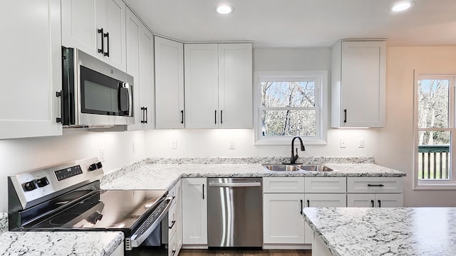 kitchen with light stone countertops, white cabinetry, appliances with stainless steel finishes, and sink