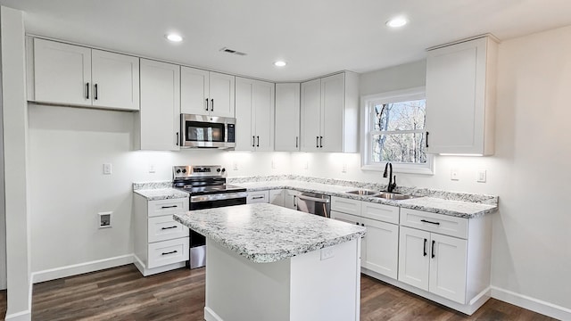 kitchen with sink, appliances with stainless steel finishes, white cabinetry, a center island, and dark hardwood / wood-style flooring