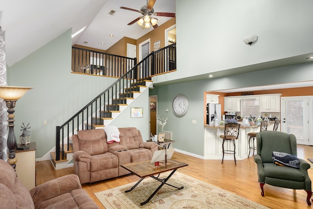 living room with ceiling fan, a towering ceiling, and light hardwood / wood-style flooring