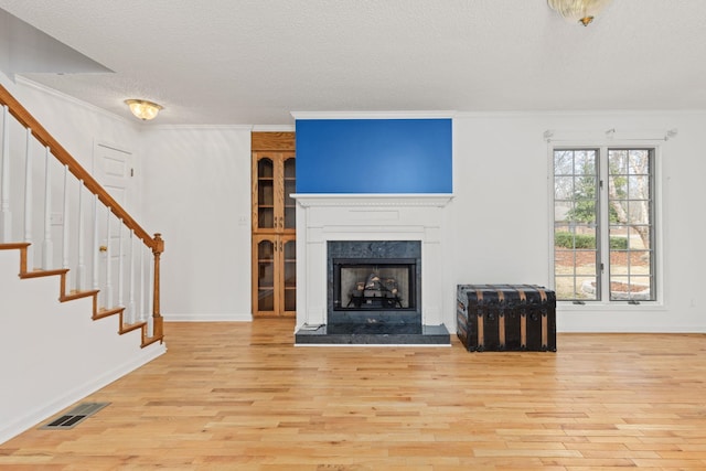 unfurnished living room with a premium fireplace, ornamental molding, a textured ceiling, and light hardwood / wood-style floors