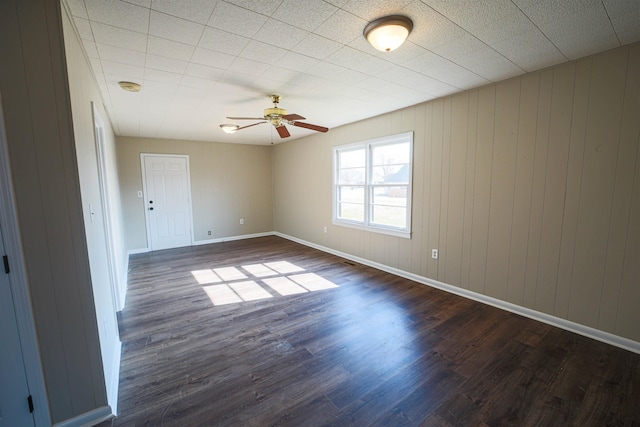 unfurnished room with dark hardwood / wood-style flooring, ceiling fan, and wood walls