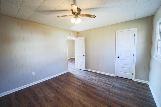 empty room with wooden walls, ceiling fan, and dark hardwood / wood-style flooring